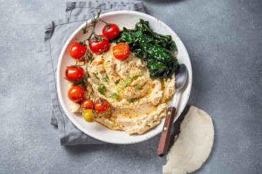 Lezzetli bir tabak kremalı humus taze domatesler, yapraklı yeşillikler ve pide ekmeğiyle servis edilir..