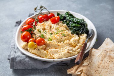Lezzetli bir tabak kremalı humus taze domatesler, yapraklı yeşillikler ve pide ekmeğiyle servis edilir..