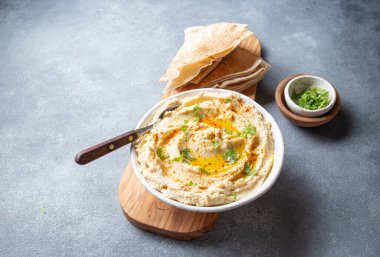 Zeytin yağı ve bitkilerle süslenmiş bir kase kremalı humus tahtadan yapılmış pide ekmeğiyle servis edilir. Ekmeğin yanına küçük bir kase garnitür yerleştirilir..