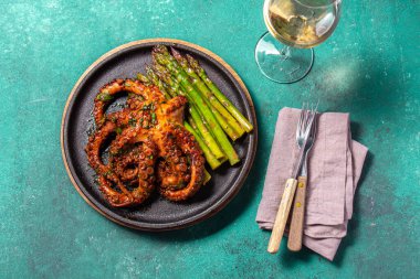 Grilled octopus with asparagus served on a black plate, highlighting vibrant colors and textures against a turquoise background. The dish is garnished with herbs, evoking a gourmet, Mediterranean feel clipart