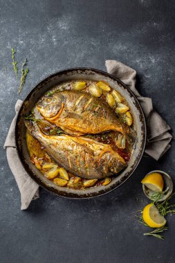 Koyu arkaplanda soğan ve otlarla pişirilmiş deniz mahsulü veya dorada..