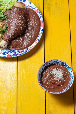 Renkli bir tabakta, marul ve pirinç garnitürlerinin yanında servis edilen zengin poblano sosuna batırılmış tavuk yer alıyor. Küçük bir kase köstebek sosu tabağa fazladan tat katar..