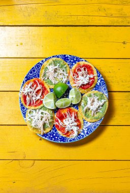 Parlak renkli chalupalar dekoratif bir tabakta düzenlenir, peynir ve parçalanmış malzemeler gibi malzemeler sergilenir. Taze kireç parçaları kutlamalar için mükemmel olan bu şenlikli Meksika yemeğine eşlik ediyor..