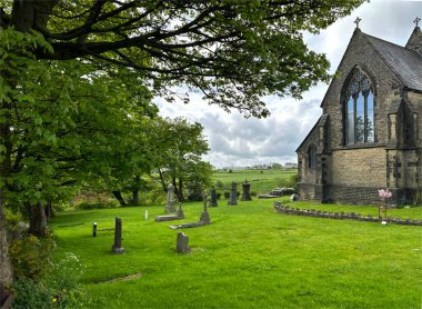 St. Aidan Kilisesi manzarası, eski ağaçlar, mezar taşları ve uzak tarlalar, bulutlu bir günde, Buttershaw, Bradford, İngiltere