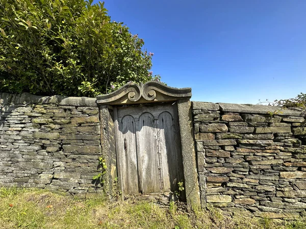 Victorian garden entrance, with ornate carved stone, and a wooden door, built into a dry stone wall in, Shelf, UK
