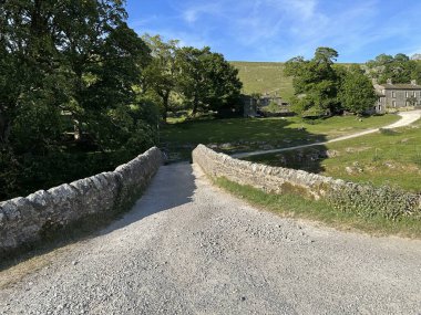 Yorkshire Dales sahnesi, küçük bir taş köprüyü geçerek, Yockenthwaite, İngiltere 'deki eski kulübelere ve çiftliklere giden bir yol.