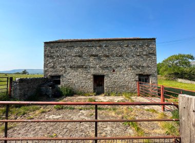 Eski Yorkshire taş ahırı, koyu kahverengi parmaklıkları ile, mavi bir gökyüzüne karşı, Bainbridge, İngiltere 'nin varoşlarında.