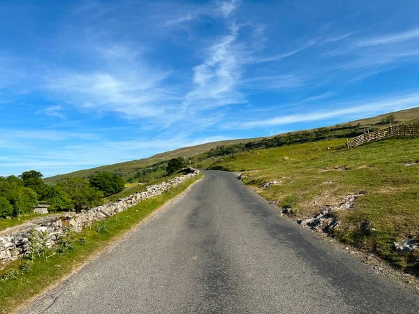 Yockenthwaite köyünün yakınından geçen yol, kuru taş duvarlar, tarlalar ve çiftliklerle, geç bir yaz gününde.