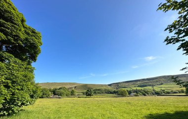Geniş açık alanlar, ağaçlar, çiftlik binaları ve yakınlarındaki uzak tepelerle manzara, Todmorden, İngiltere
