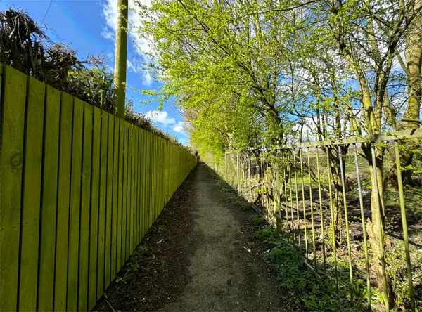 英国同城谢克利夫巷 一条狭窄的土路延伸到左边明亮的绿色木栅栏和右边有幼树的金属栏杆之间 免版税图库照片