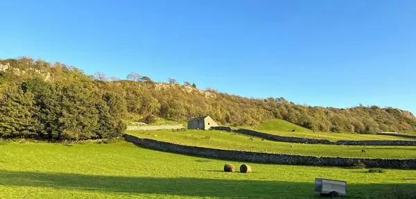 静谧的风景沐浴在温暖的阳光下 一座孤零零的建筑矗立在英国塞德尔郡Stainforth的绿色田野和干枯的石墙中 图库图片