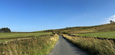 Moor Yolu, yemyeşil çayırlarla ve açık mavi gökyüzünün altındaki kuru taş duvarlarla çevrili olan mesafeye kadar uzanır. Manzara, İngiltere 'de Elslack, Skipton, İngiltere' de sakin ve kırsal bir atmosfer taşır.