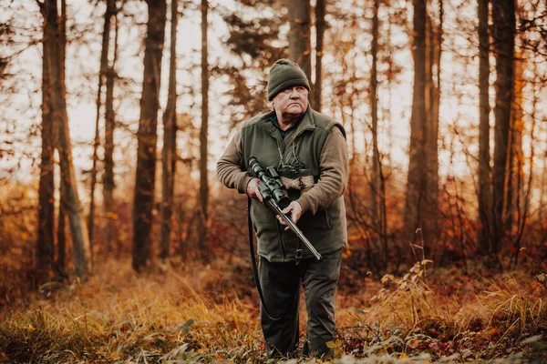 Autumn hunting season, hunter with rifle looking out for some wild animal in a wood or forest, outdoor sports concept