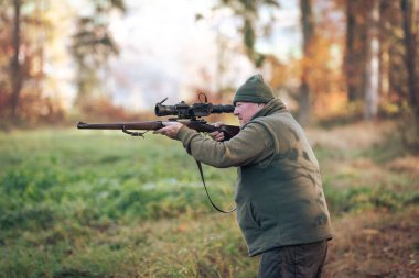 Autumn hunting season, hunter with rifle looking out for some wild animal in wood or forest, outdoor sports concept