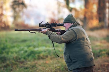 Autumn hunting season, hunter with rifle looking out for some wild animal in wood or forest, outdoor sports concept