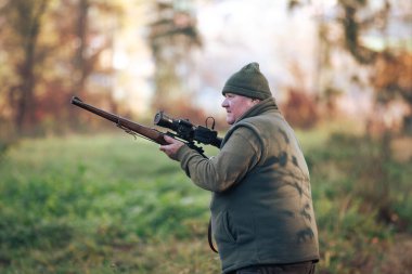 Autumn hunting season, hunter with rifle looking out for some wild animal in wood or forest, outdoor sports concept