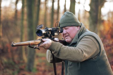 Autumn hunting season, hunter with rifle looking out for some wild animal in wood or forest, outdoor sports concept