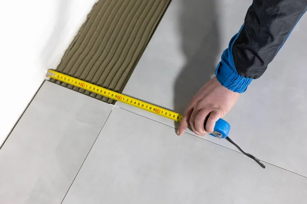 Tiler worker placing or tiling gray ceramic tile in position over adhesive glue with lash tile leveling system, renovation or recontruction, concept of building