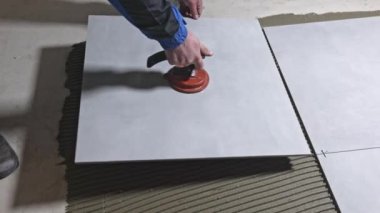 Tiler worker placing or tiling gray ceramic tile in a position over adhesive glue with lash tile leveling system, renovation or recontruction, concept of building