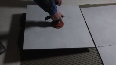 Tiler worker placing or tiling gray ceramic tile in a position over adhesive glue with lash tile leveling system, renovation or recontruction, concept of building