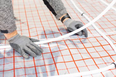 Worker installing underfloor heating system, water heating on new residential house, concept of heated floor