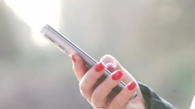 Young woman typing by mobile phone outdoors during lovely sunset, Close up hand with smartphone in an urban background, lady holding cellphone in hands outside, technology concept