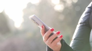 Gün batımında dışarıda cep telefonuyla yazı yazan genç bir kadın, şehir arka planında akıllı bir telefonla el ele tutuşan bir kadın, dışarıda cep telefonunu tutan bir kadın, teknoloji kavramı.
