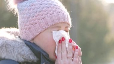 Young woman sneezing in the tissue, blowing runny nose with symptoms cold during winter time and freezing weather, illness concept