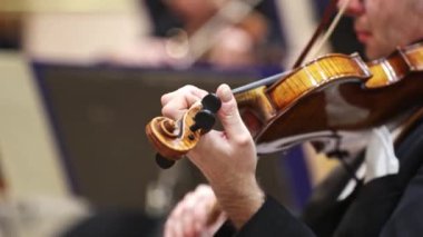 Profesyonel senfoni orkestrası sahnede konser veriyor ve klasik müzik konseri çalıyor, kemancı ön planda.