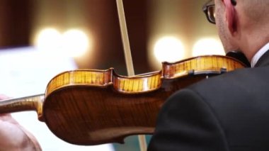 Profesyonel senfoni orkestrası sahnede konser veriyor ve klasik müzik konseri çalıyor, kemancı ön planda.