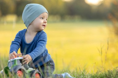 Genç çocuk güneşli bir çayırda oyuncak bir traktörle oynuyor, sıcak havanın ve temiz havanın tadını çıkarıyor.