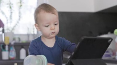 Yüzünde yemek olan genç bir çocuk tablet bilgisayara bakıyor.