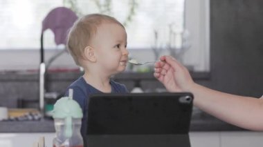 Annesi bebeğini beslerken o tablet bilgisayarı izliyor.