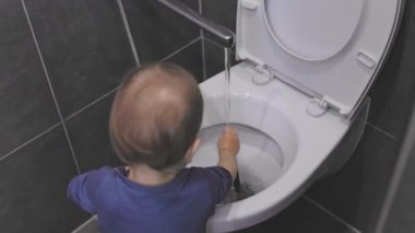 Genç çocuk modern bir tuvaletin klozetinde suyla oynuyor.