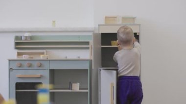Bebek, dolaplar ve aletlerle deney yaparken renkli bir oyuncak mutfak setiyle meşgul oluyor.