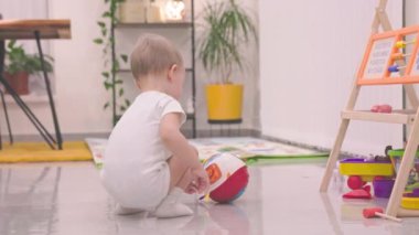 Modern bir oyun odasında yerde renkli bir eğitim topuyla oynayan sevimli erkek bebek.