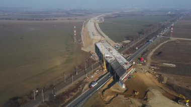 İnşaat işçileri ve mühendisleri kırsal bir arazinin üzerine bir otoyol üstgeçit köprüsü inşa ediyorlar.