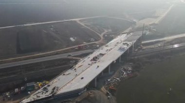 İnşaat işçileri bir otoyol üst geçidi inşa ederek, prefabrik beton bölümlerin sürmekte olan montajını sergiliyorlar.