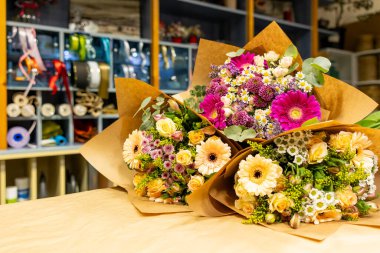 İçinde güller, gerberalar ve papatyalar bulunan canlı buketler çiçekçilerin çalışma alanından satın alınmaya hazır.