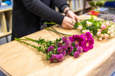 Çiçekçi kağıt kaplı ahşap bir masada pembe ve mor bir çiçek buketi hazırlıyor.