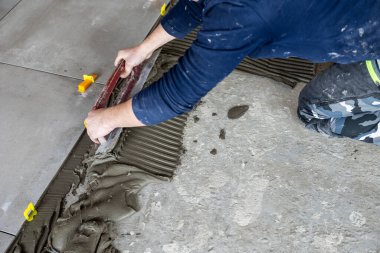 Tiler seramik fayansları yere yerleştiriyor, çentik mala ve fayans boşlukları kullanarak.