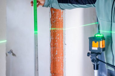 Ev yenileme sırasında düzgün ölçümler için çapraz hat lazer seviyesi ve cetvel kullanan inşaatçı