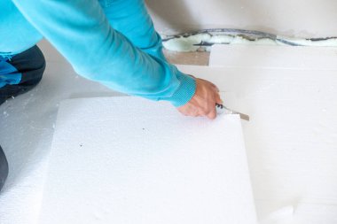 İnşaat işçisi, zemin yalıtım işi sırasında bıçak kullanarak strafor yalıtım tahtasını kesiyor.