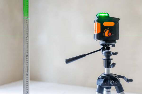 Laser level projecting green beam onto ruler during a construction or renovation project in an empty room