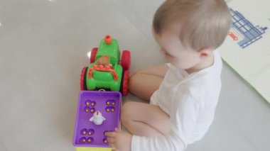 Oyuncak bir traktör ve römorkla meşgul olan küçük oyuncak hayvanları yerleştirip kaldıran küçük bir çocuk.