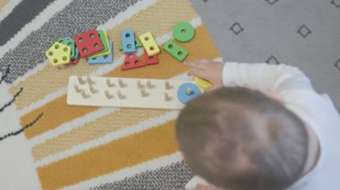 Bebek tahtadan bir geometrik şekil ayırıcı oyuncakla oynuyor, iyi motor beceriler ve problem çözme yetenekleri geliştiriyor.