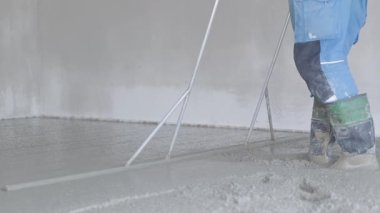 İşçi bir inşaat projesinde düz ve pürüzsüz bir yüzey sağlamak için zemine eşit miktarda ıslak beton yaymak için düz bir araç kullanır.