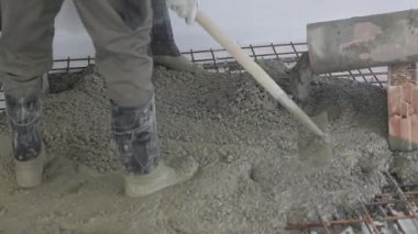 İnşaat işçisi ustalıkla çelik takviyesinin üzerine kürek kullanarak taze beton döker. Beton temel inşa etmek için pürüzsüz bir yüzey oluşturmak için eşit olarak dökülüyor