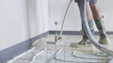 İnşaat işçisi alt kattaki ısıtma sistemini kapatmak için sıvı tornavida dolduruyor. Hassas zemin düzleştiriliyor