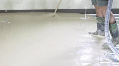 İnşaat işçisi ustalıkla zemine sıvı çimento dökerek pürüzsüz ve eşit bir yüzey için gerekli becerileri gösteriyor.